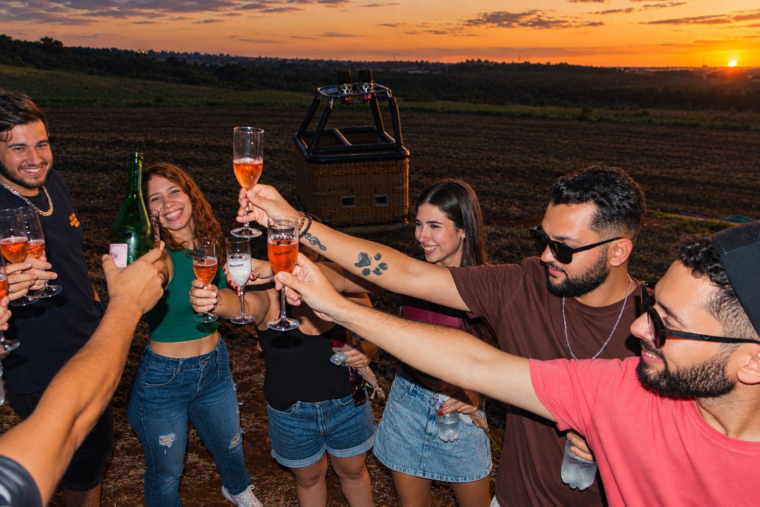 Grupo de amigos brindando com espumante ao lado do cesto do balão ao pôr do sol