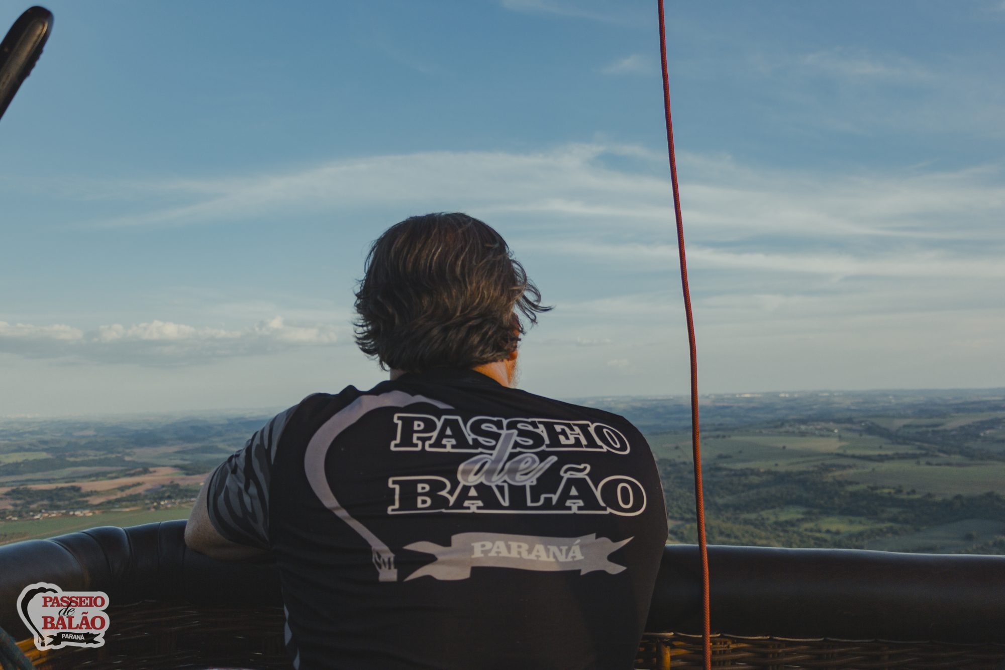 Piloto com a camiseta da empresa olhando a paisagem do cesto